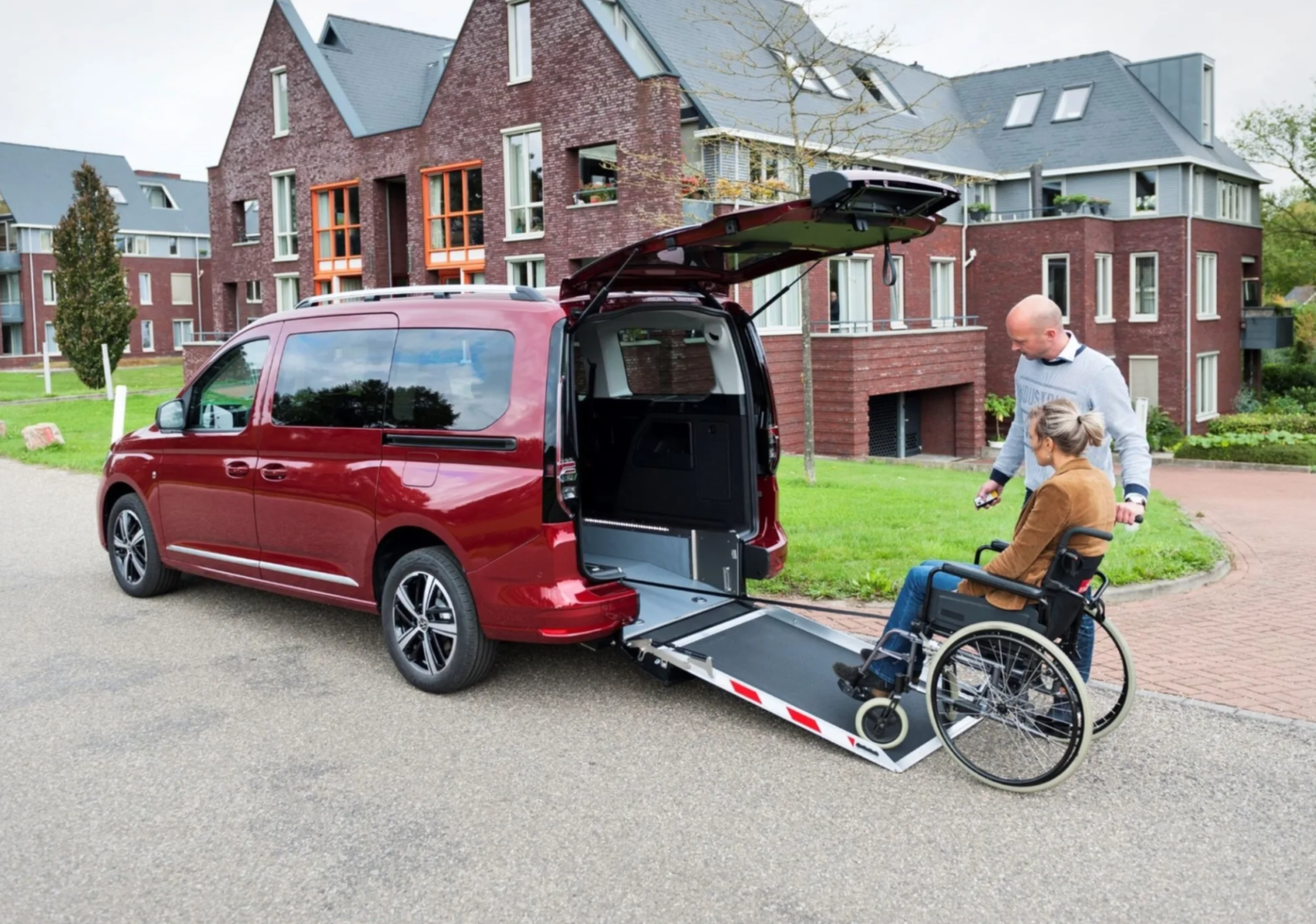 Een auto met een aanpassing voor een rolstoel en twee personen die hier gebruik van maken.